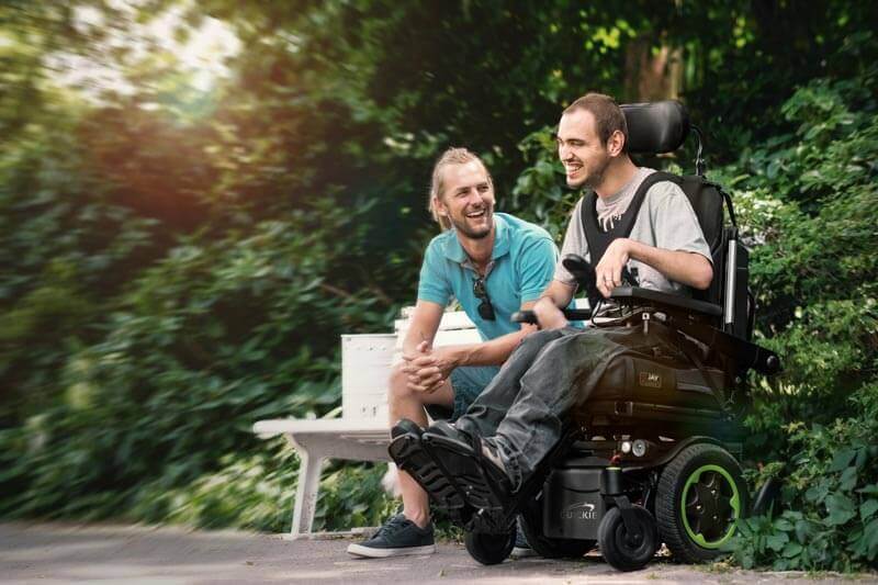 A man using a power wheelchair, hanging out with a friend