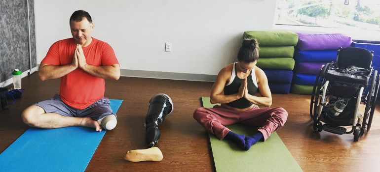 A woman who uses a wheelchair and a man with a leg amputation practice yoga together